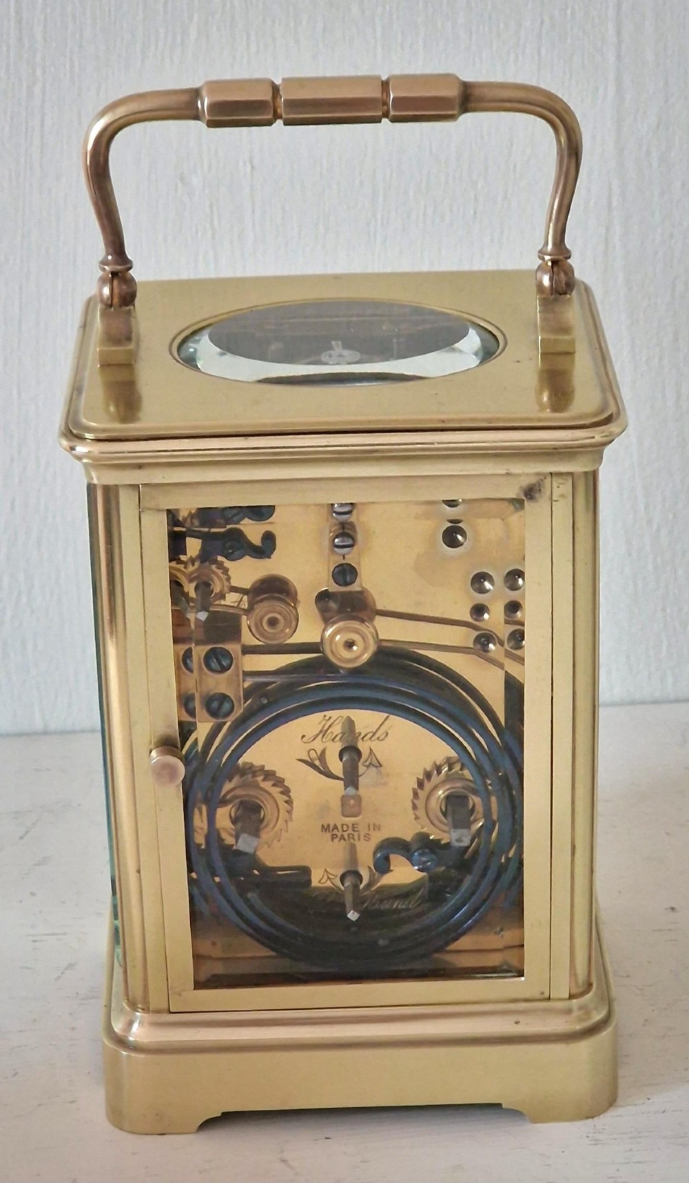 A French brass carriage clock with a top carrying handle, white enamel dial with Roman numerals, and clear glass side panels. View II
