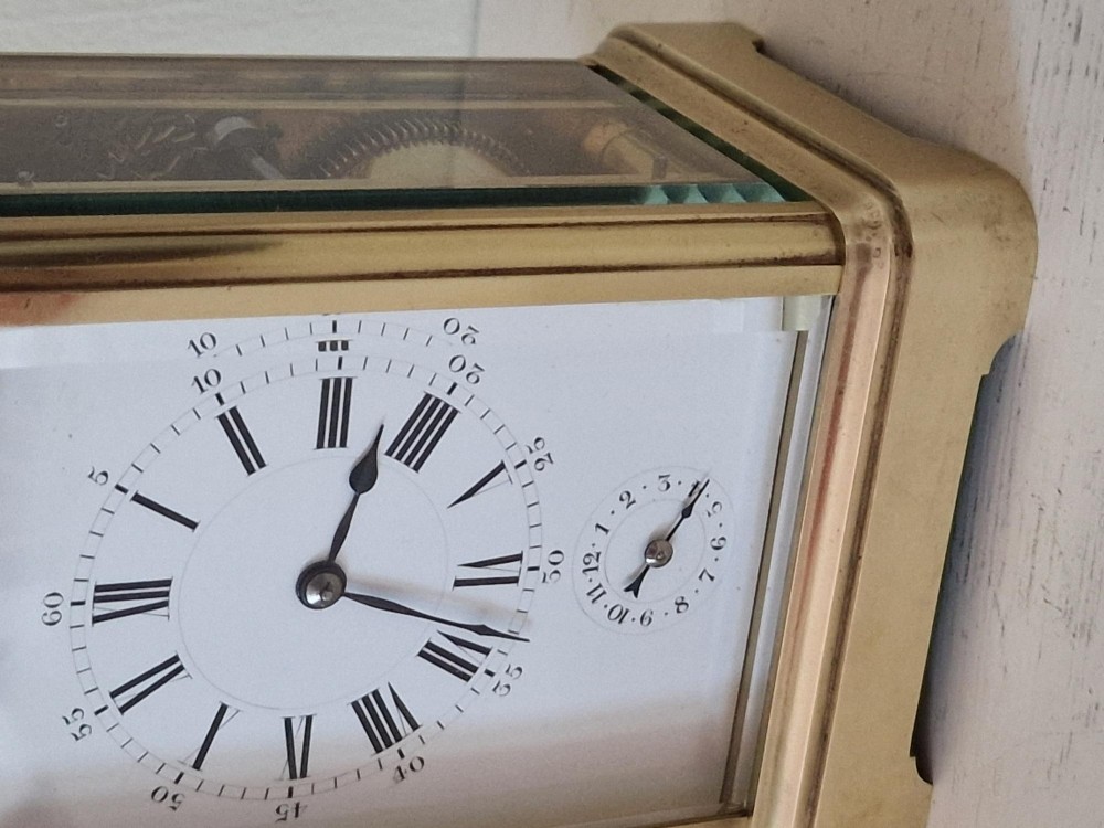 A French brass carriage clock with a top carrying handle, white enamel dial with Roman numerals, and clear glass side panels. View V