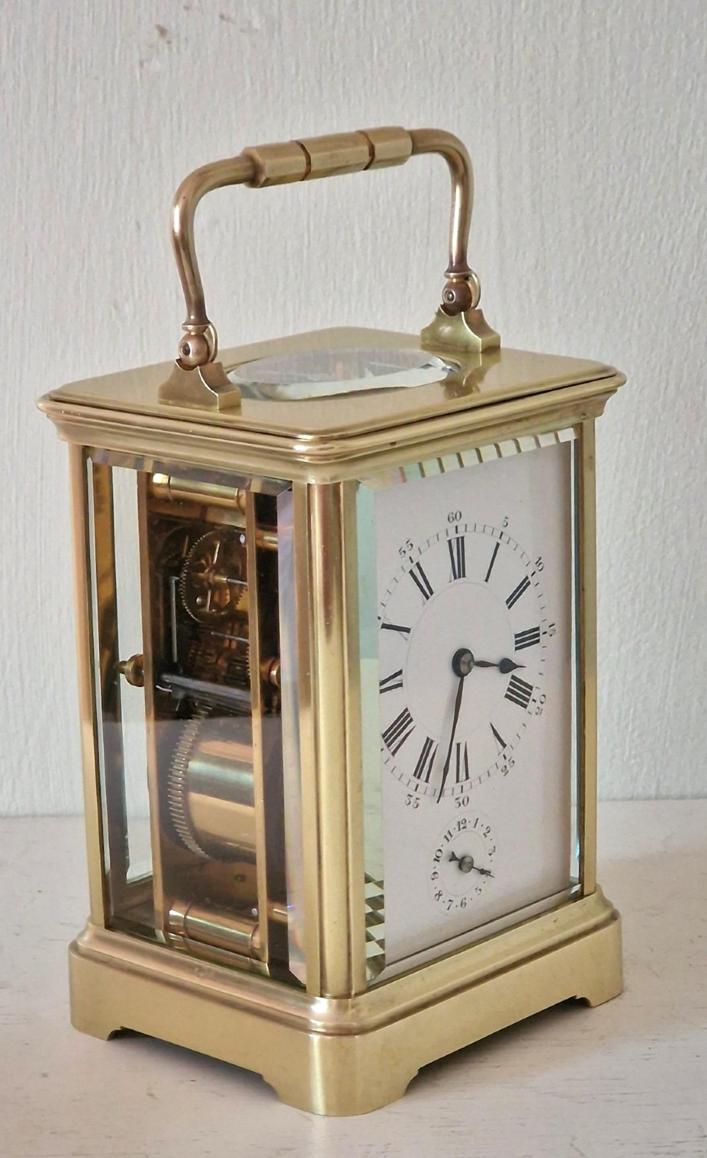 A French brass carriage clock with a top carrying handle, white enamel dial with Roman numerals, and clear glass side panels. View VI