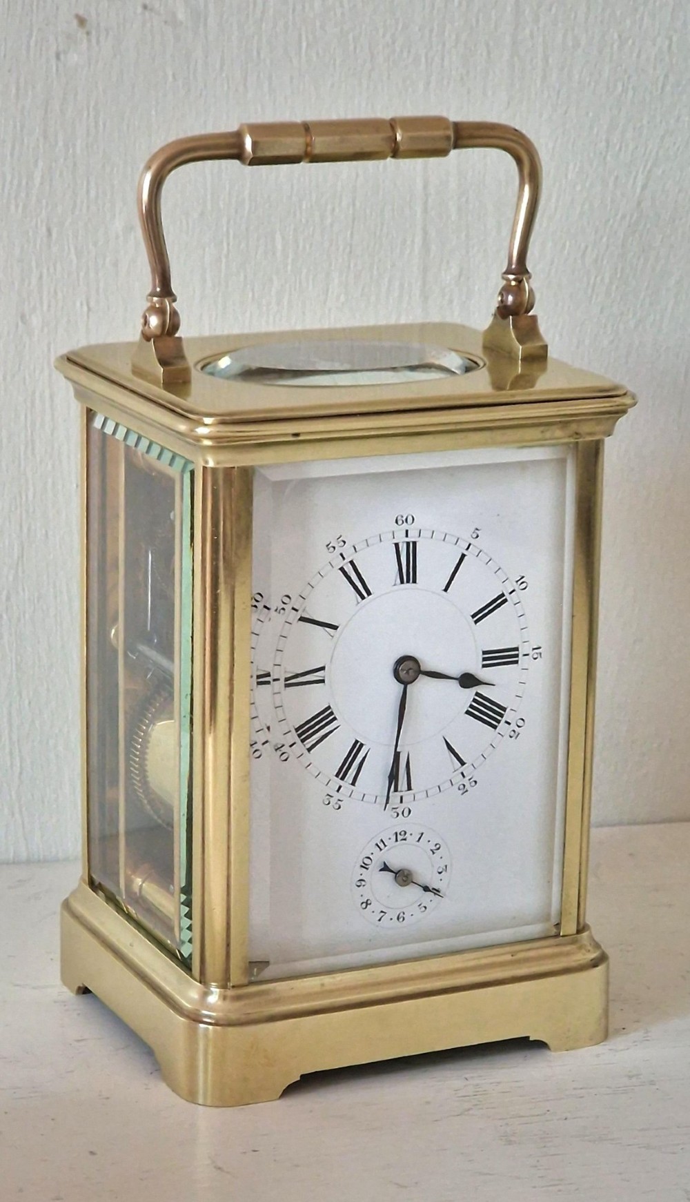 A French brass carriage clock with a top carrying handle, white enamel dial with Roman numerals, and clear glass side panels. View VII