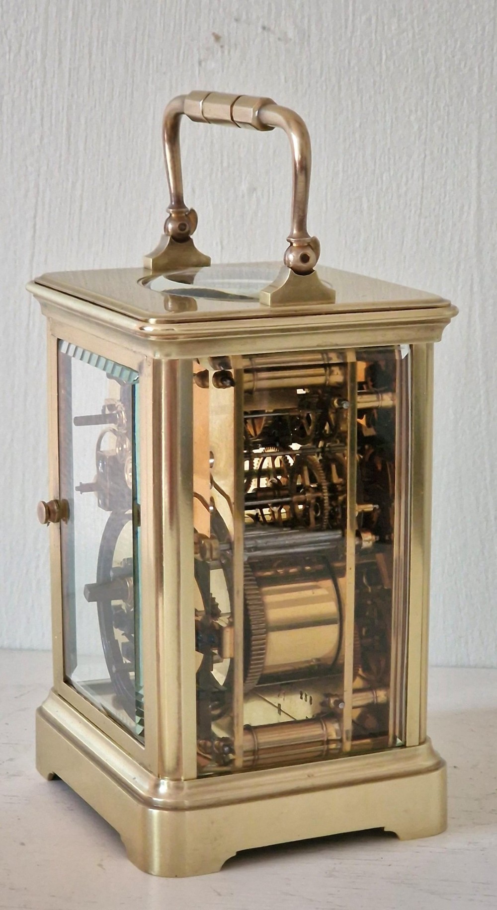 A French brass carriage clock with a top carrying handle, white enamel dial with Roman numerals, and clear glass side panels. View VIII