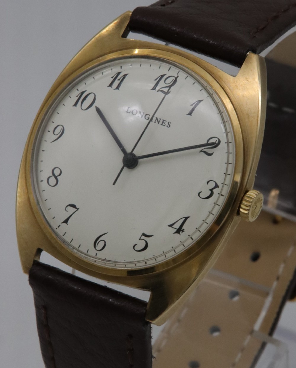 A 1974 Longines wristwatch with a cushion-shaped 9k yellow gold case, a white dial with black Arabic numerals, and a brown leather strap. View II