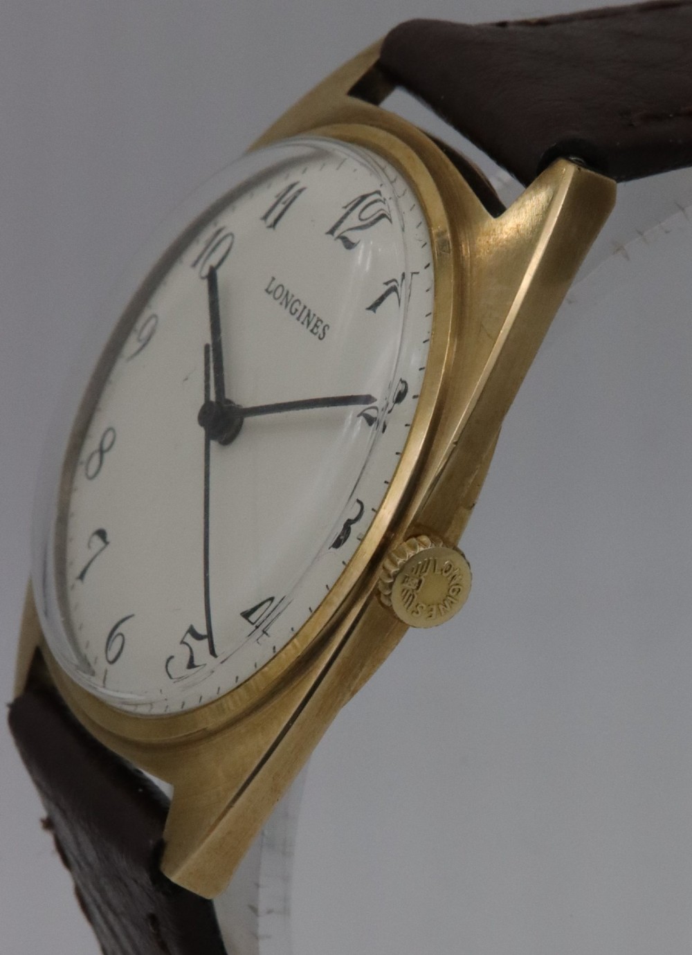 A 1974 Longines wristwatch with a cushion-shaped 9k yellow gold case, a white dial with black Arabic numerals, and a brown leather strap. View III