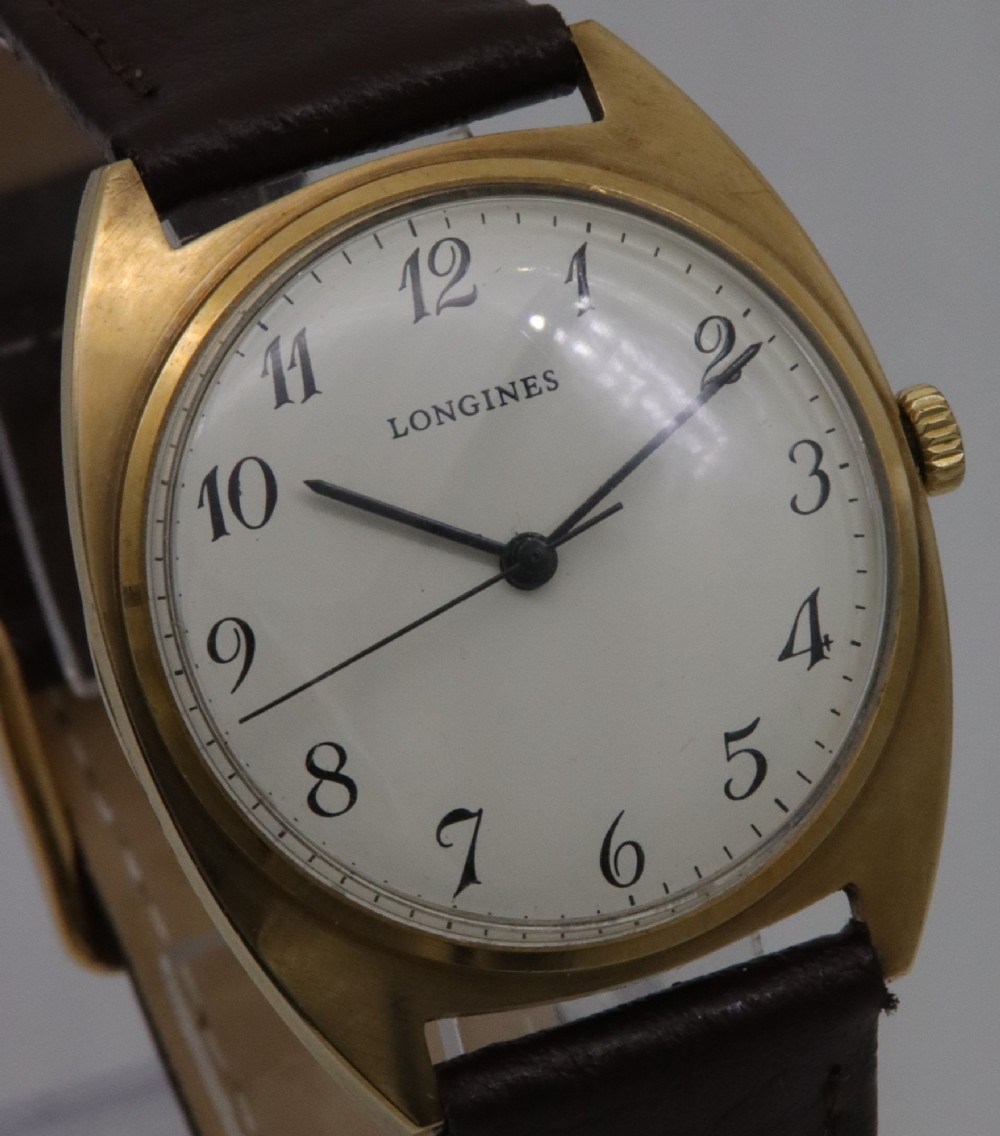 A 1974 Longines wristwatch with a cushion-shaped 9k yellow gold case, a white dial with black Arabic numerals, and a brown leather strap. View IV