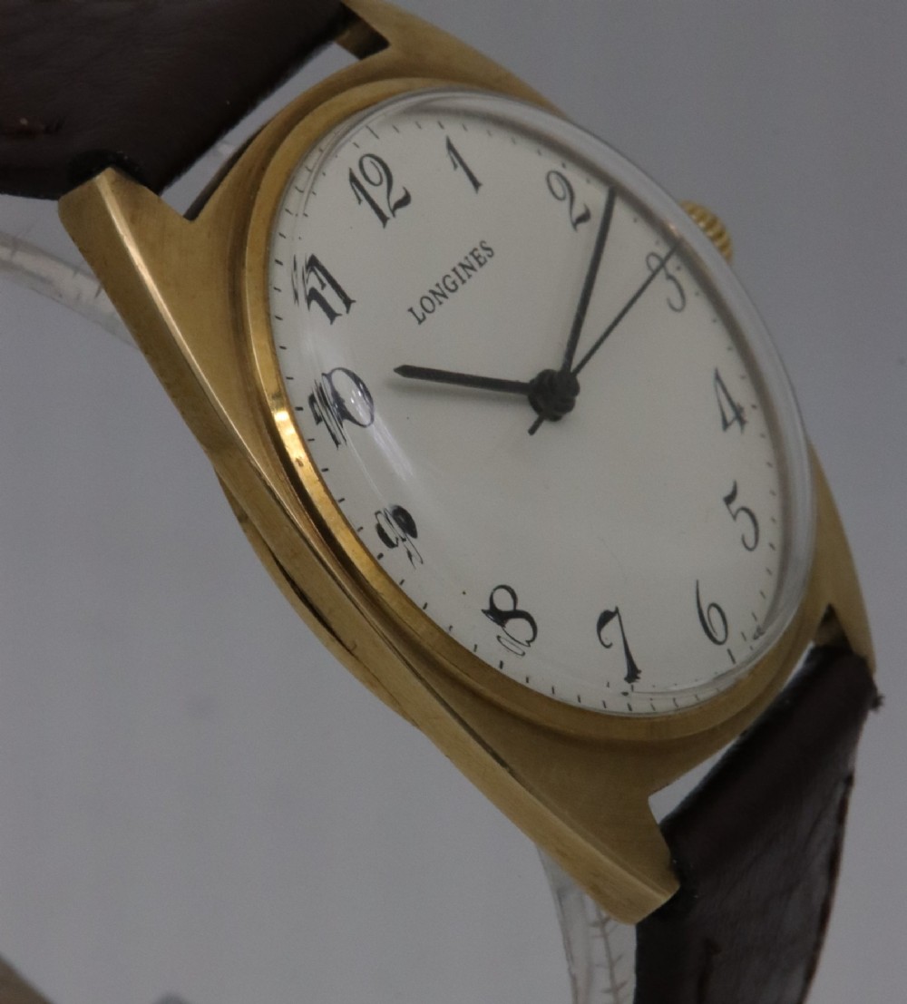 A 1974 Longines wristwatch with a cushion-shaped 9k yellow gold case, a white dial with black Arabic numerals, and a brown leather strap. View V