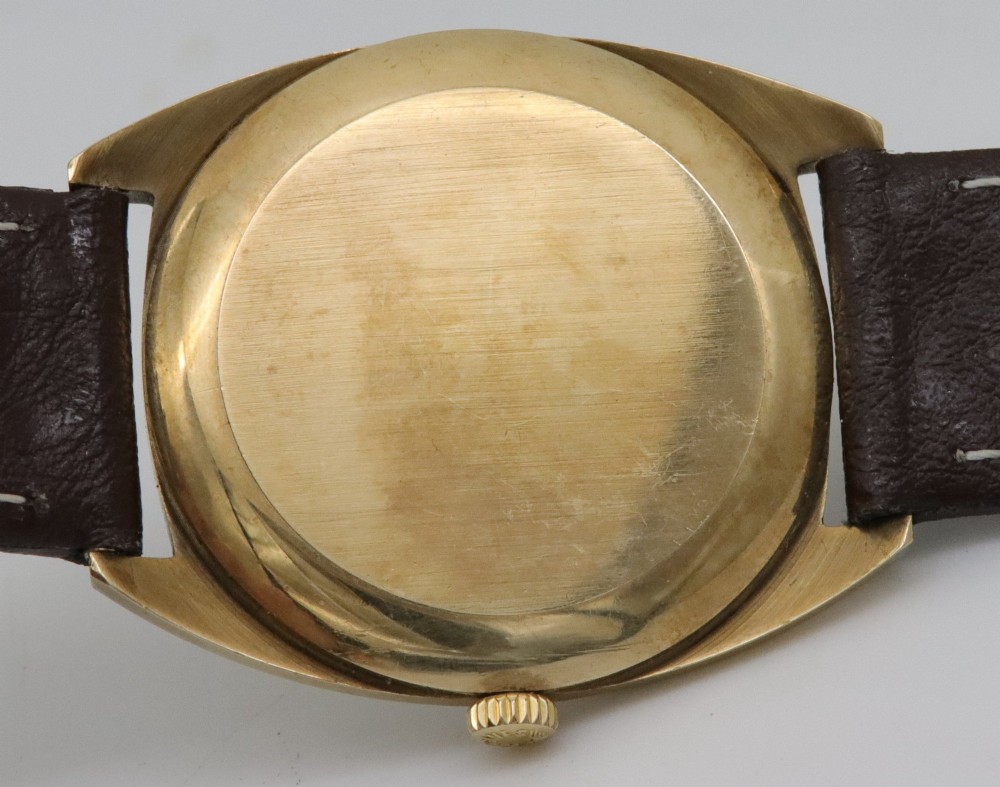 A 1974 Longines wristwatch with a cushion-shaped 9k yellow gold case, a white dial with black Arabic numerals, and a brown leather strap. View VI