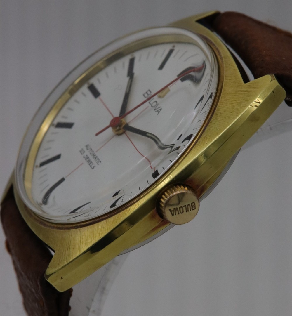 A 1970s Bulova automatic wristwatch featuring a gold-toned cushion case, a white crosshair dial with black markers, and a brown leather strap. View III