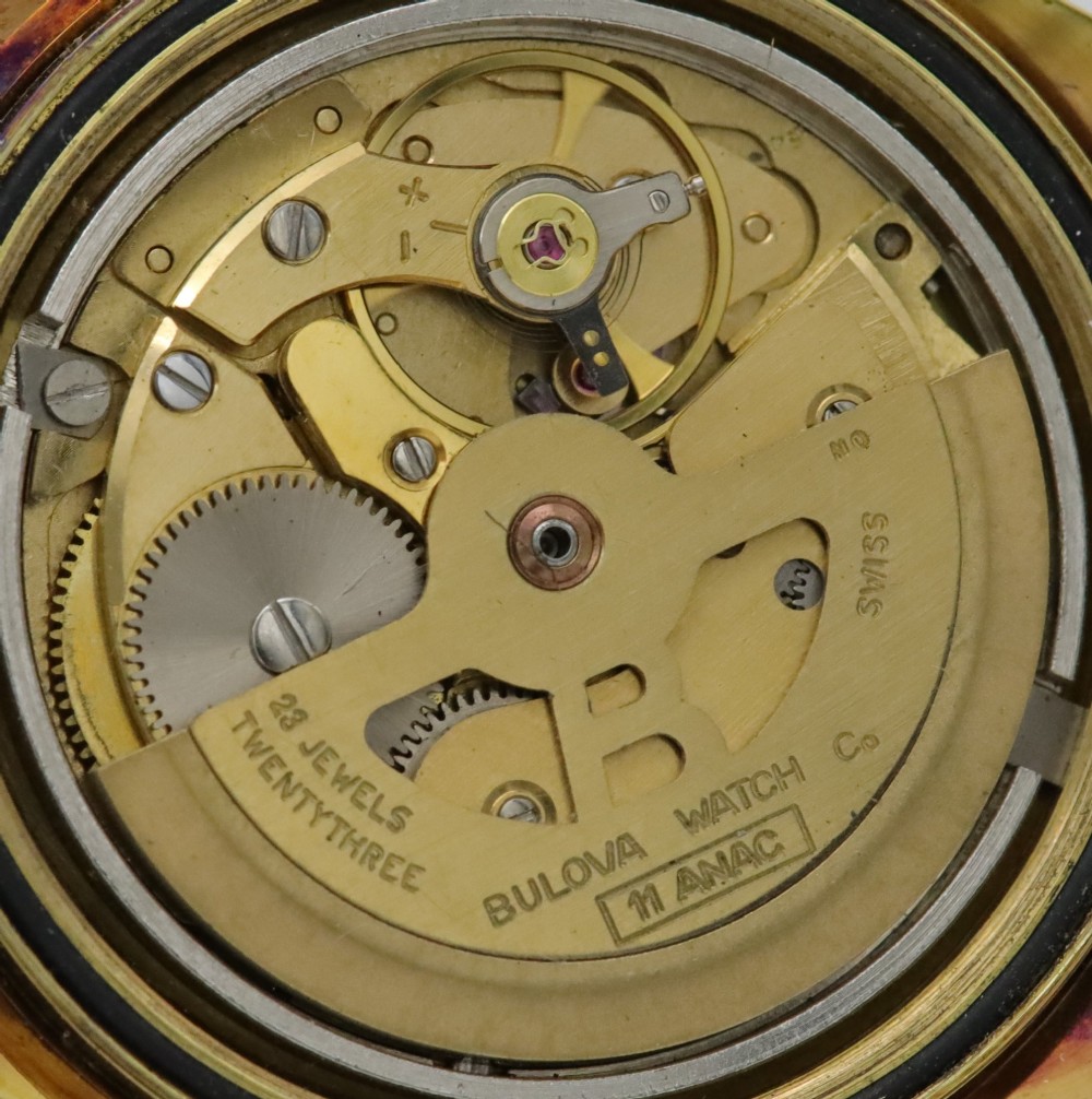 A 1970s Bulova automatic wristwatch featuring a gold-toned cushion case, a white crosshair dial with black markers, and a brown leather strap. View VII