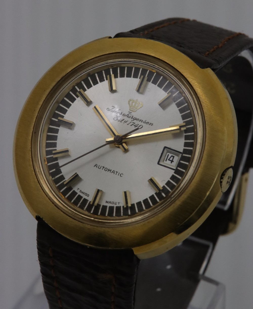 A 1970s Jules Jurgensen automatic wristwatch with a gold-toned circular cushion case, white dial, date aperture, and brown textured leather strap. View II