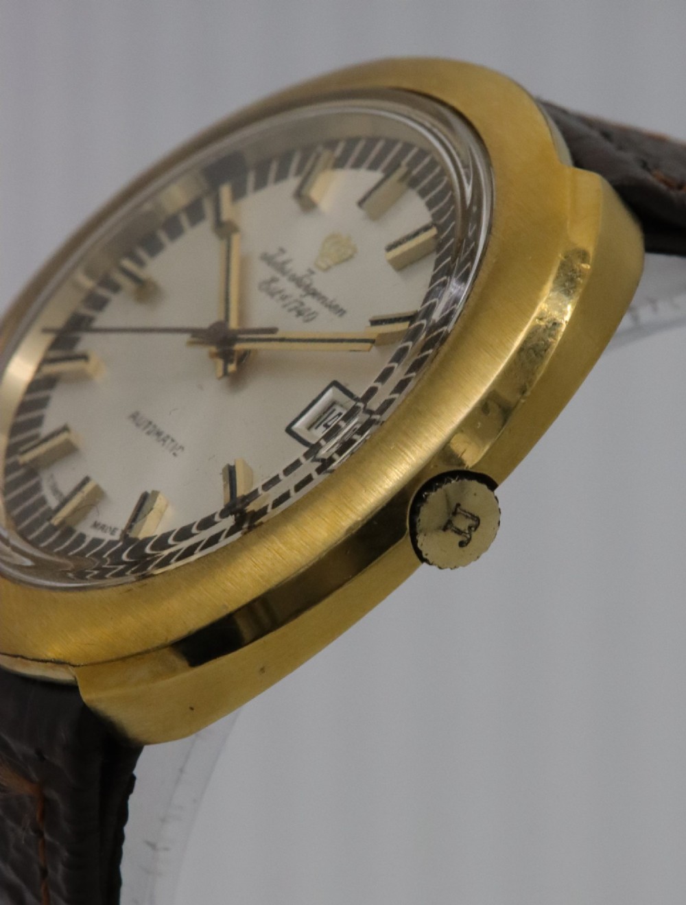 A 1970s Jules Jurgensen automatic wristwatch with a gold-toned circular cushion case, white dial, date aperture, and brown textured leather strap. View III