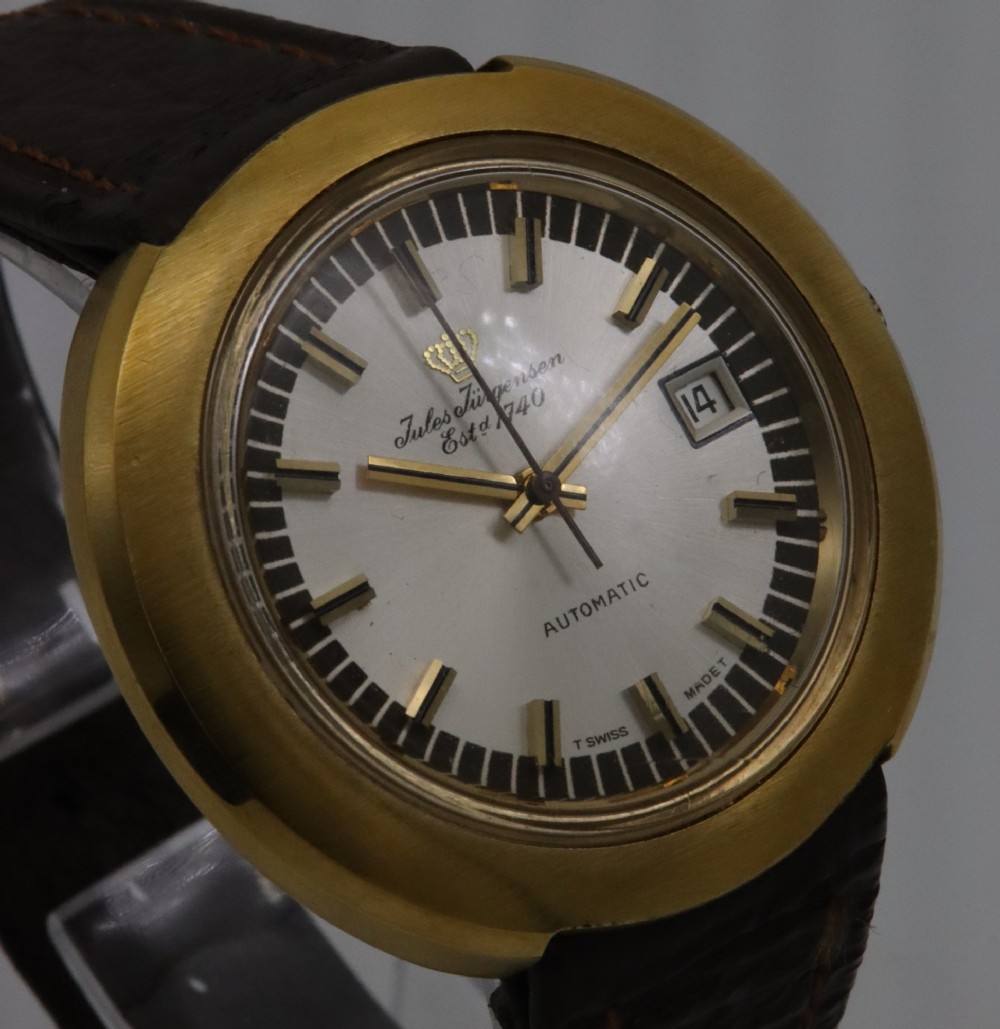 A 1970s Jules Jurgensen automatic wristwatch with a gold-toned circular cushion case, white dial, date aperture, and brown textured leather strap. View IV