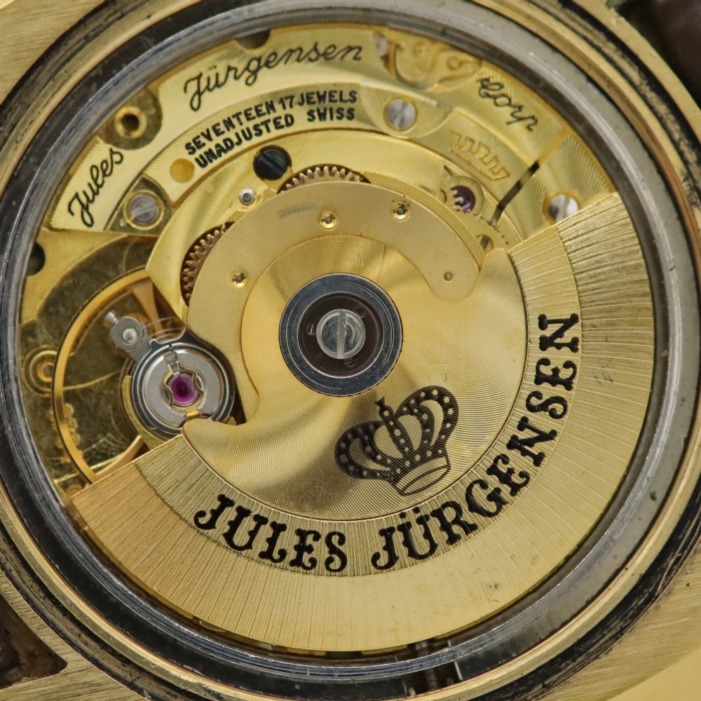 A 1970s Jules Jurgensen automatic wristwatch with a gold-toned circular cushion case, white dial, date aperture, and brown textured leather strap. View VII