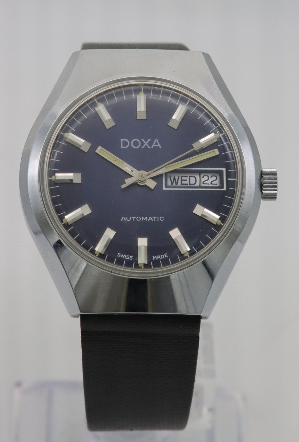 A 1970s Doxa automatic wristwatch featuring a cushion-shaped stainless steel case, blue dial with day-date aperture, and black strap.