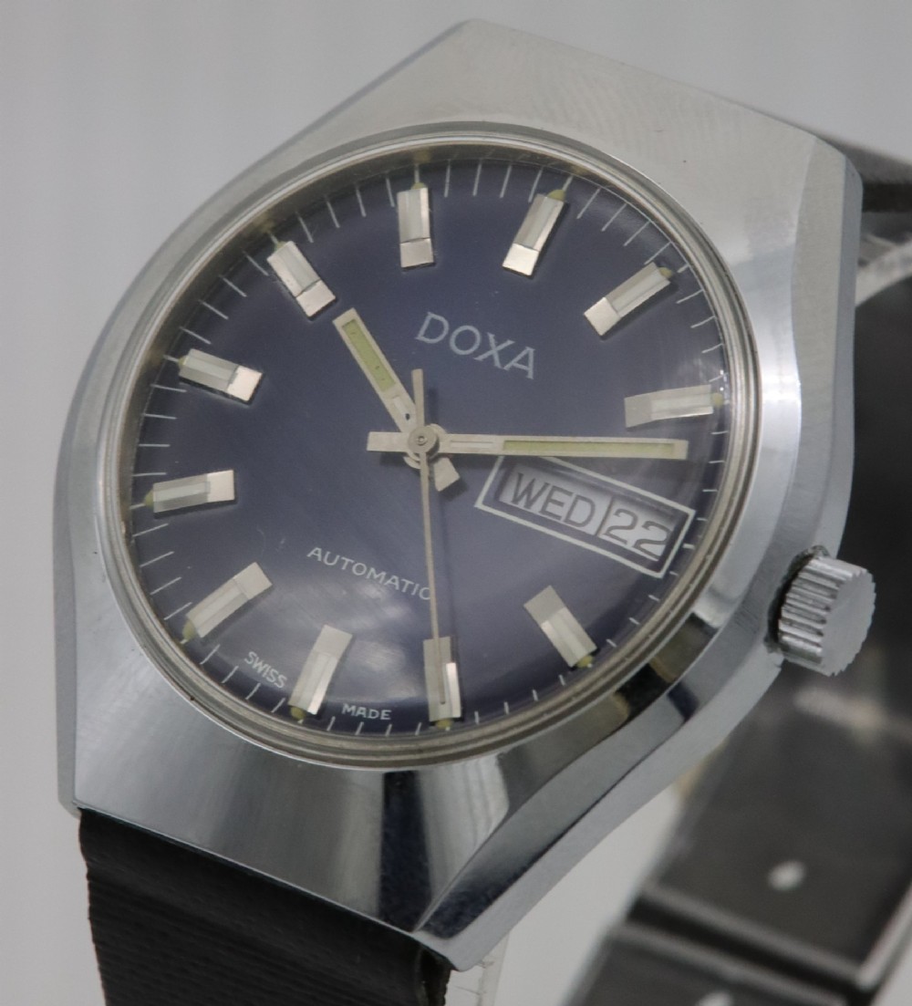 A 1970s Doxa automatic wristwatch featuring a cushion-shaped stainless steel case, blue dial with day-date aperture, and black strap. View II