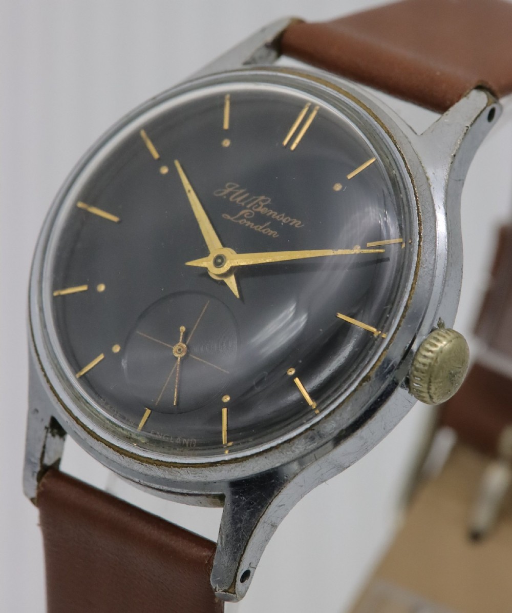 A 1950s J.W. Benson wristwatch featuring a black dial, gold-toned hands, a sub-seconds subdial at six oclock, a metallic case, and a smooth brown leather strap. View II
