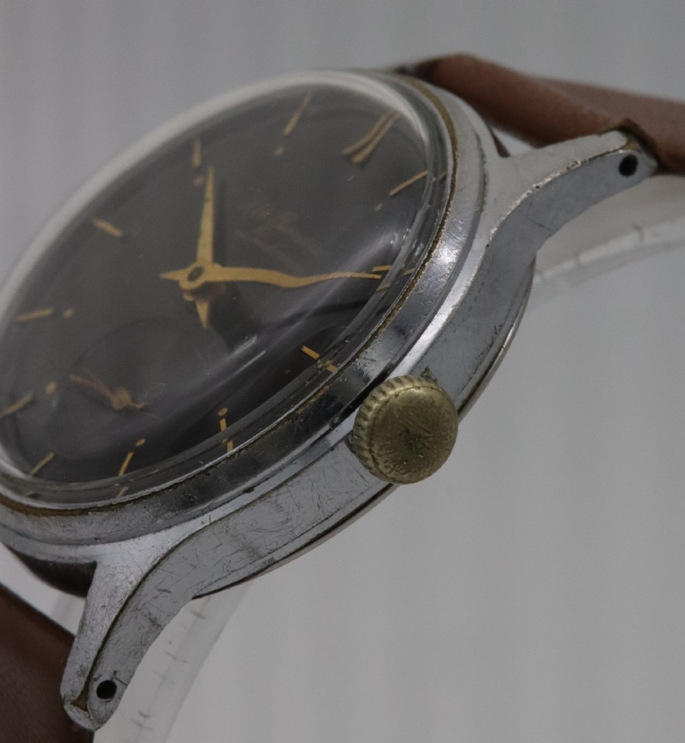 A 1950s J.W. Benson wristwatch featuring a black dial, gold-toned hands, a sub-seconds subdial at six oclock, a metallic case, and a smooth brown leather strap. View III