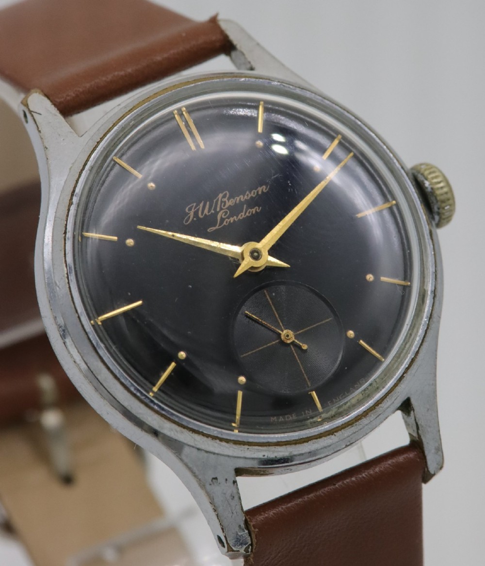 A 1950s J.W. Benson wristwatch featuring a black dial, gold-toned hands, a sub-seconds subdial at six oclock, a metallic case, and a smooth brown leather strap. View IV