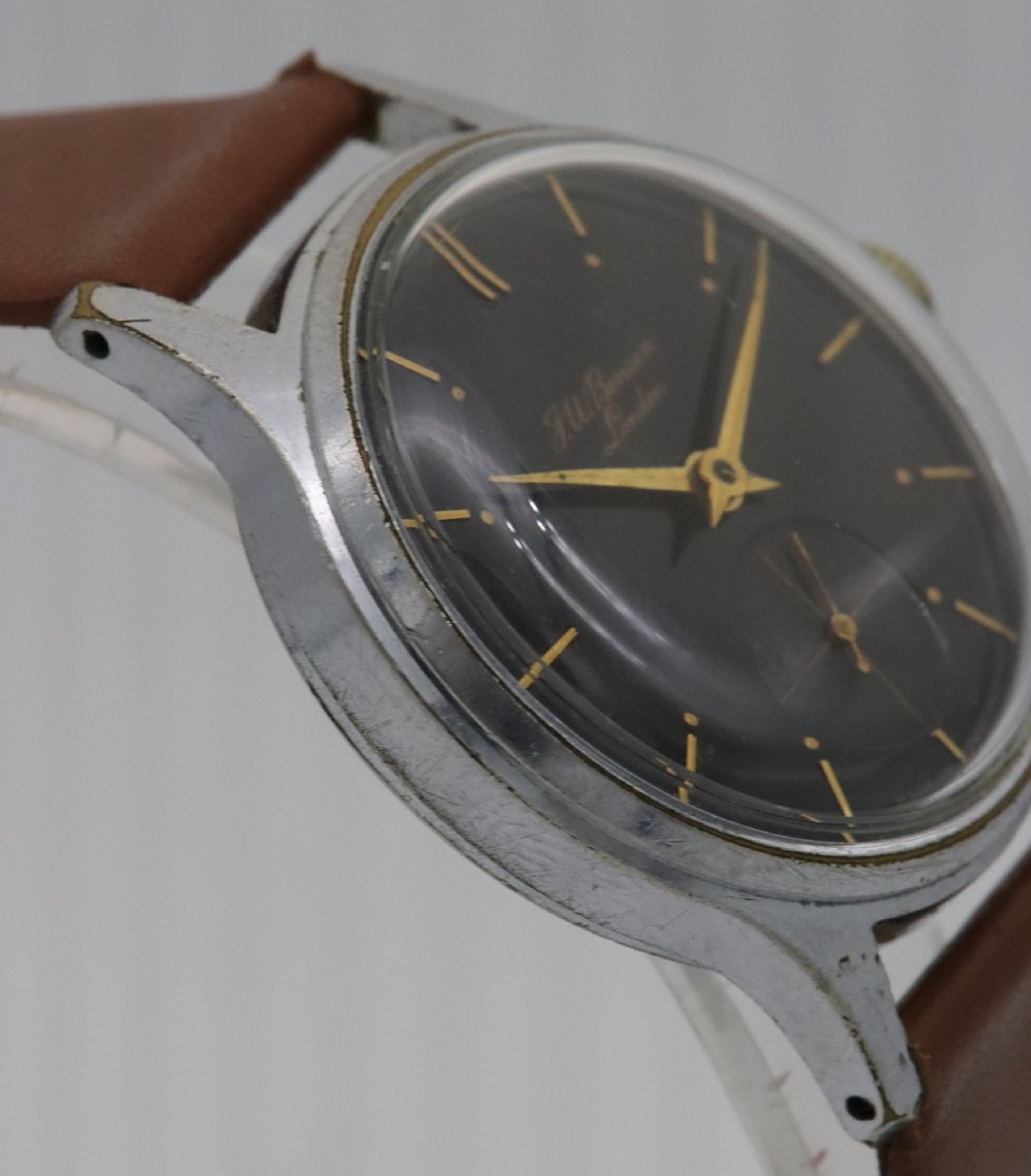 A 1950s J.W. Benson wristwatch featuring a black dial, gold-toned hands, a sub-seconds subdial at six oclock, a metallic case, and a smooth brown leather strap. View V