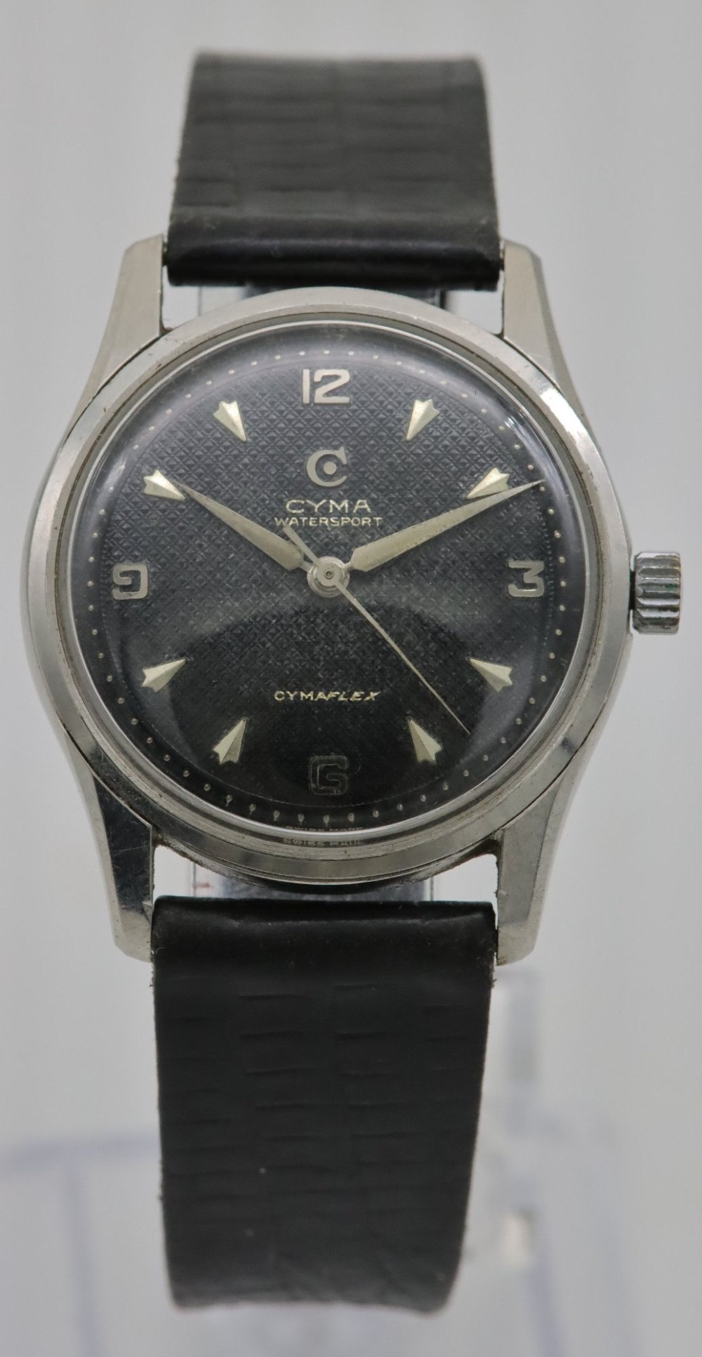 A 1950s Cyma Watersport Cymaflex wristwatch featuring a round stainless steel case, a black textured waffle dial with silver markers, and a black strap.