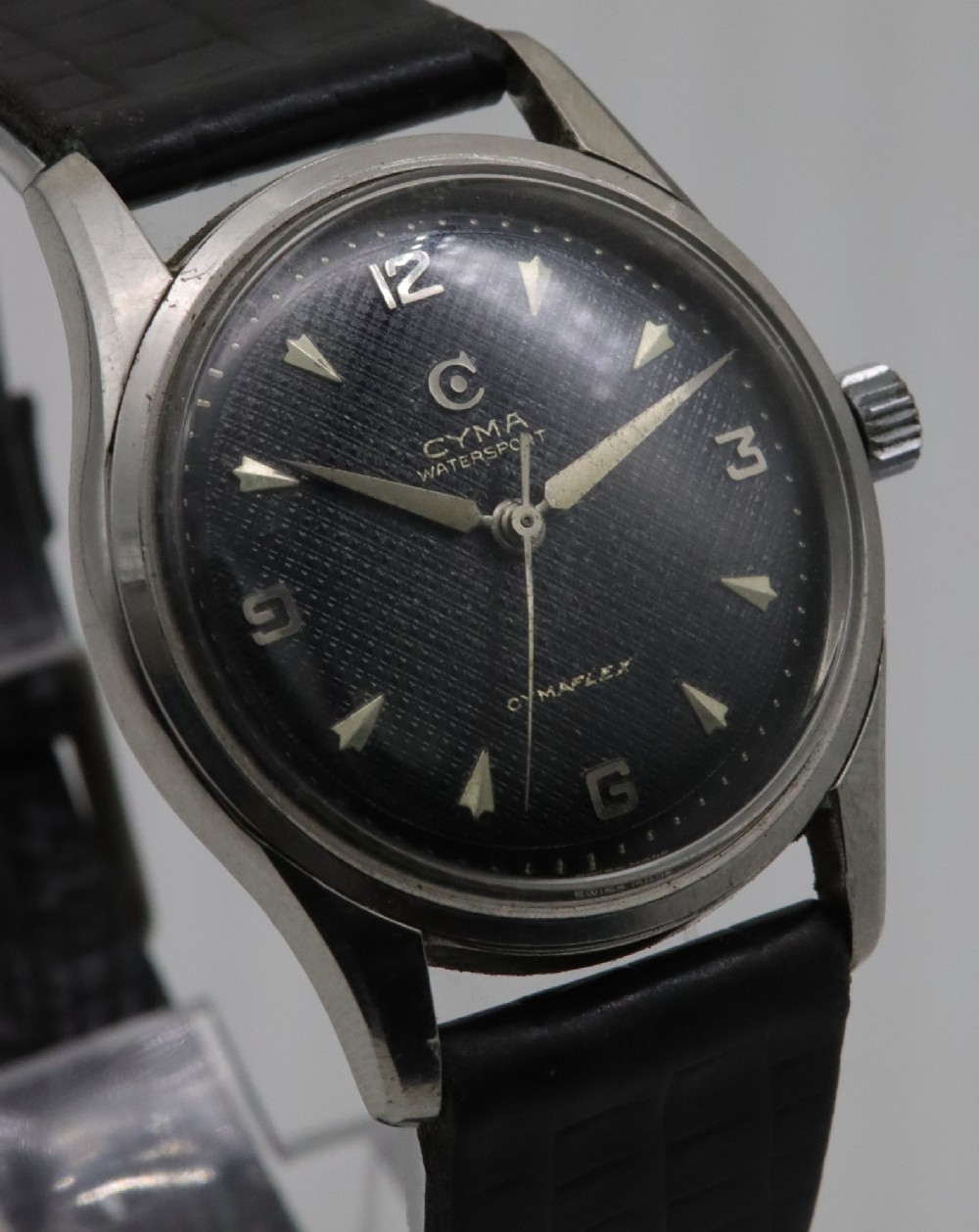 A 1950s Cyma Watersport Cymaflex wristwatch featuring a round stainless steel case, a black textured waffle dial with silver markers, and a black strap. View III