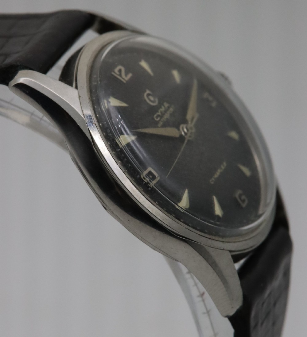 A 1950s Cyma Watersport Cymaflex wristwatch featuring a round stainless steel case, a black textured waffle dial with silver markers, and a black strap. View IV