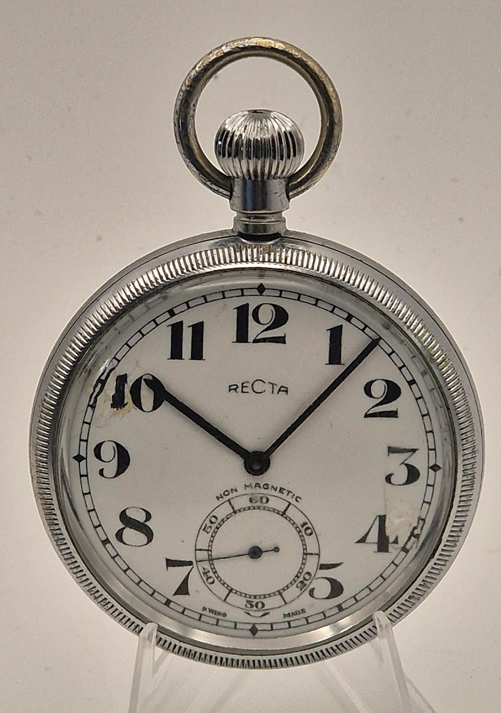 An open-face vintage pocket watch with a silver-toned metal casing, white enamel dial displaying bold black Arabic numerals, and a small sub-seconds dial.