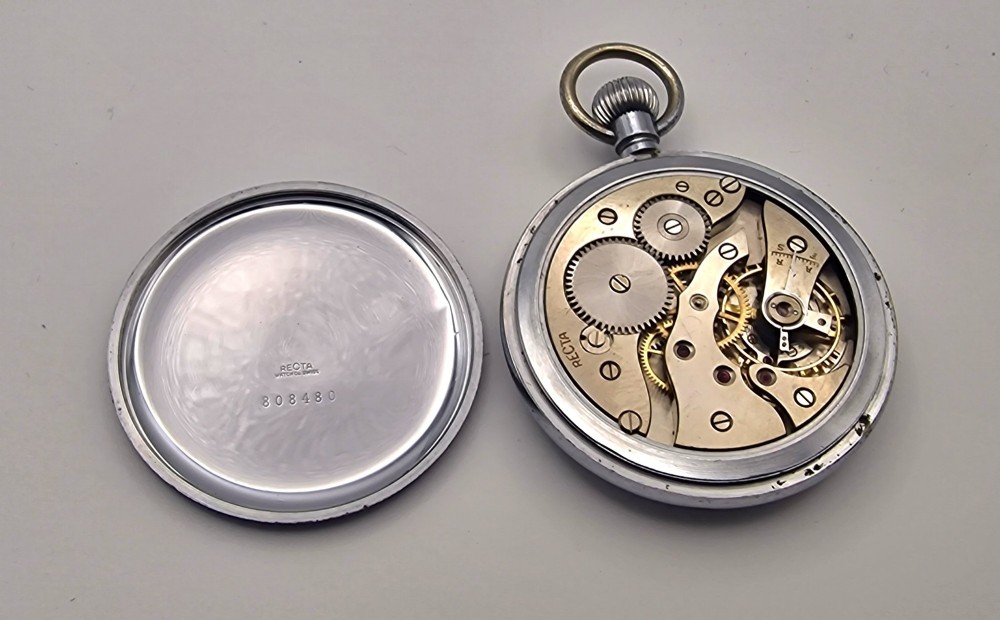 An open-face vintage pocket watch with a silver-toned metal casing, white enamel dial displaying bold black Arabic numerals, and a small sub-seconds dial. View III