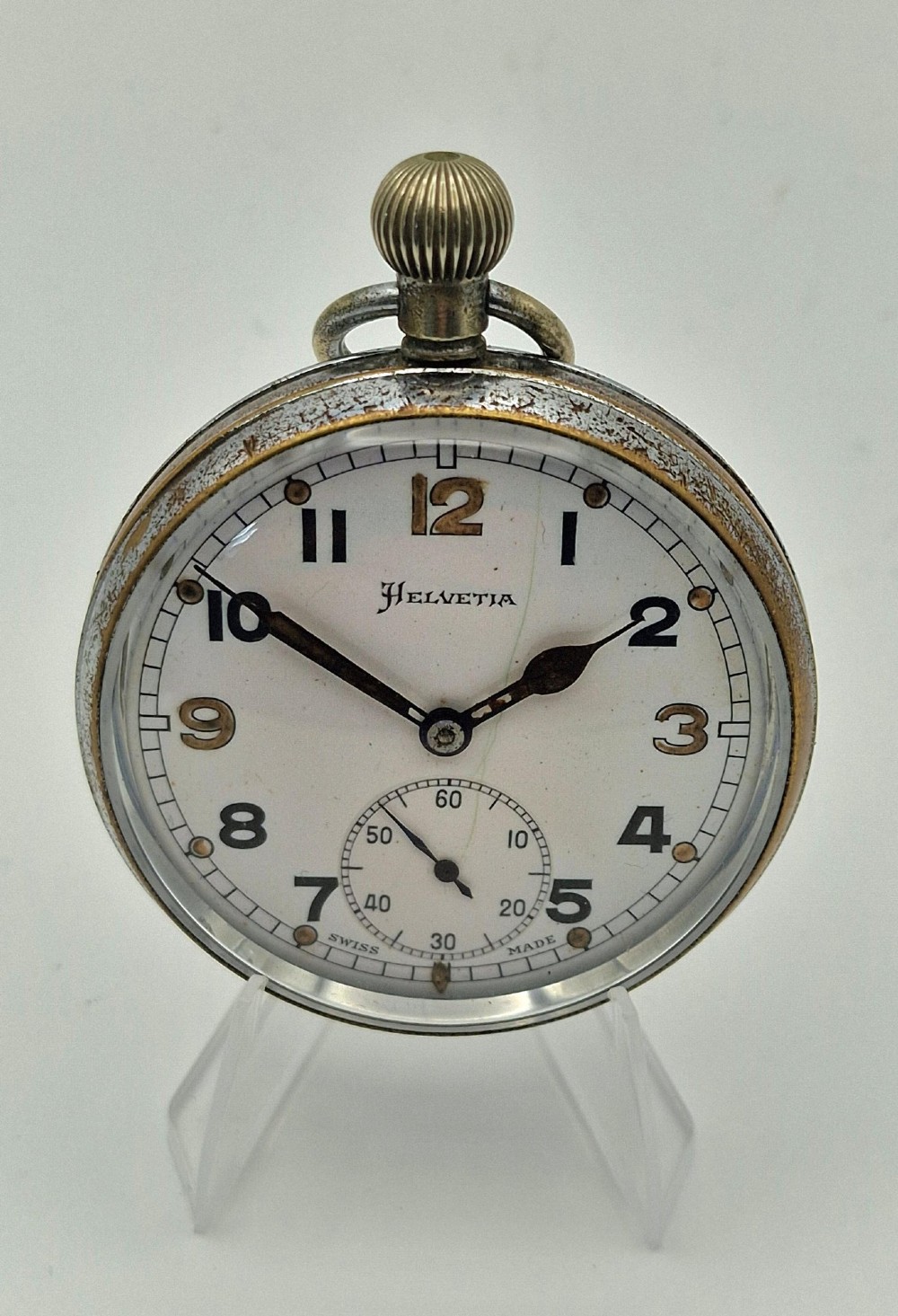 A round Helvetia military pocket watch featuring a white dial with bold black numbers, a sub-seconds dial, and a worn metal casing.