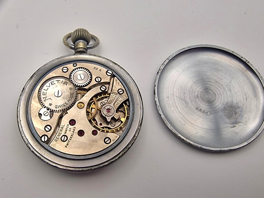 A round Helvetia military pocket watch featuring a white dial with bold black numbers, a sub-seconds dial, and a worn metal casing. View III