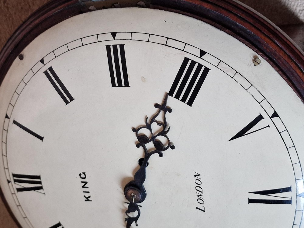 A circular Georgian fusee wall clock with a dark mahogany bezel surround, off-white painted dial featuring Roman numerals, ornate black hands, and signed King London. View II