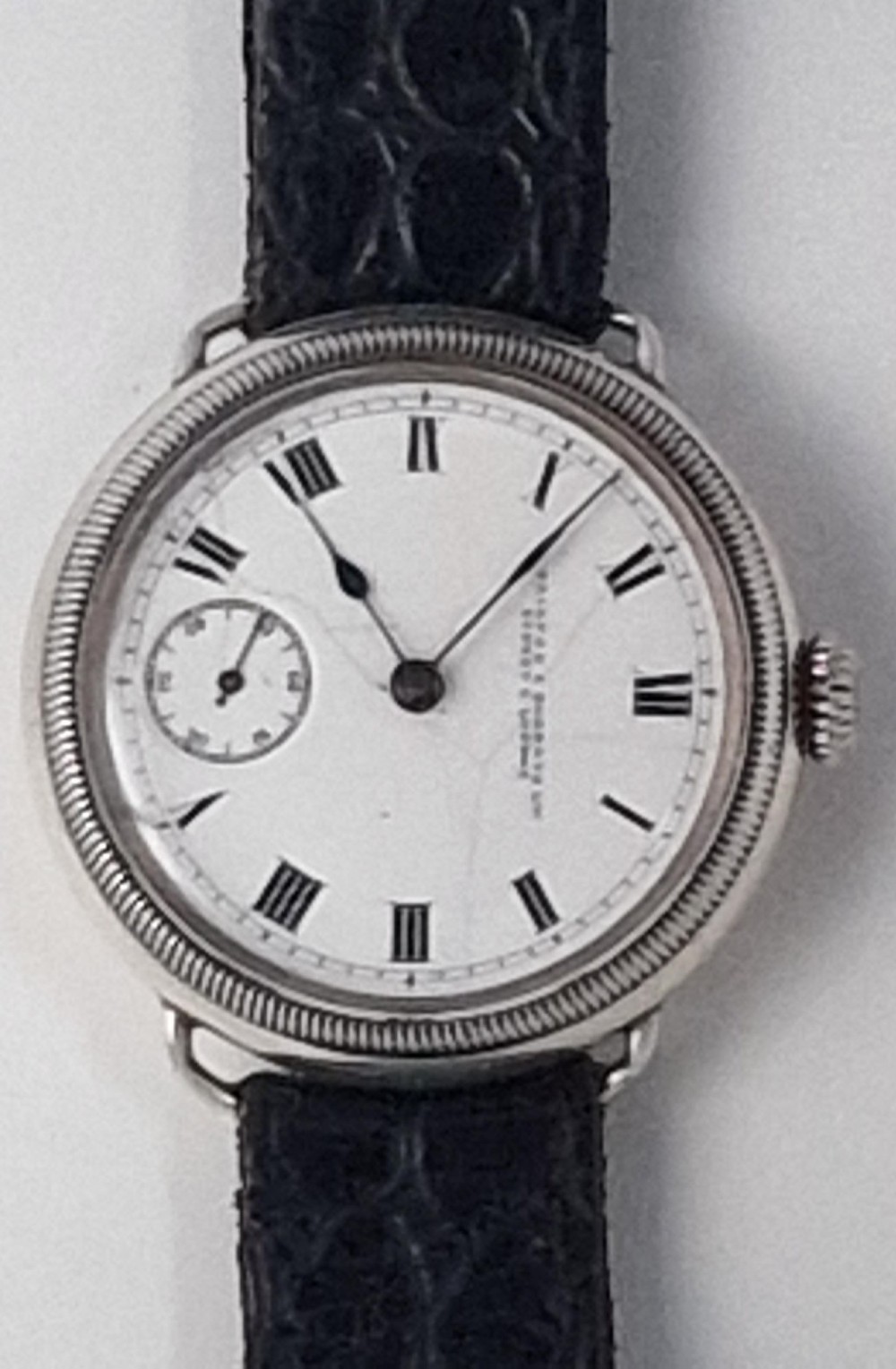A 1934 Omega pilot wristwatch featuring a white enamel dial with Roman numerals, an offset sub-seconds dial, blued steel hands, a coin-edge bezel, and a black leather strap. View III