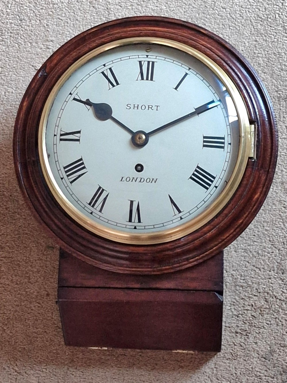 An antique wall clock featuring a circular white dial marked Short London with Roman numerals, housed in a moulded mahogany wooden casing with a brass-framed glass bezel.