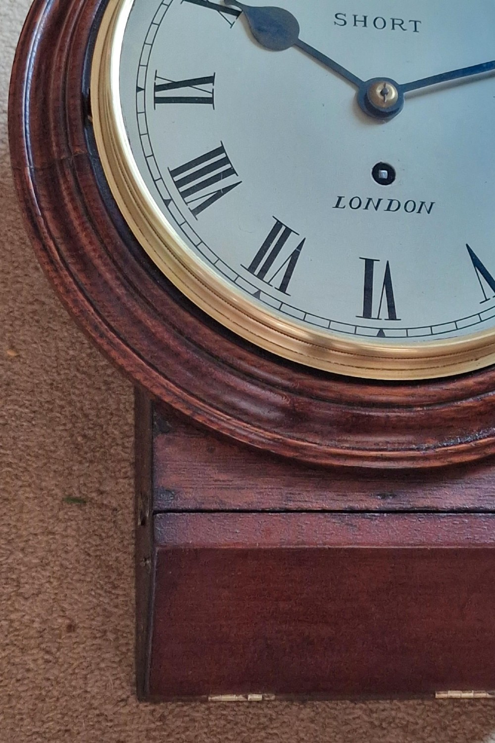 An antique wall clock featuring a circular white dial marked Short London with Roman numerals, housed in a moulded mahogany wooden casing with a brass-framed glass bezel. View III