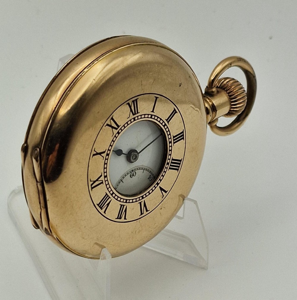 A gold-coloured half-hunter pocket watch featuring an outer case with black Roman numerals around a central glass viewing aperture. View III