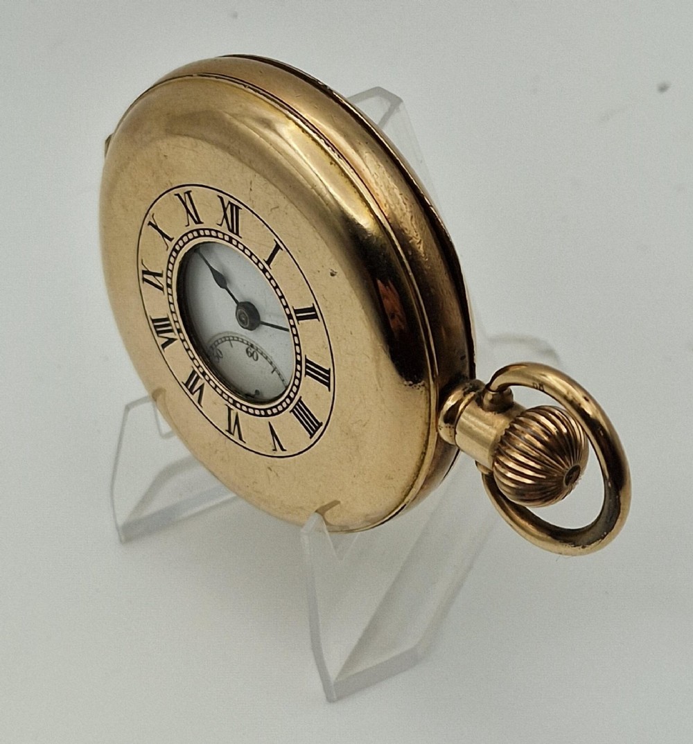 A gold-coloured half-hunter pocket watch featuring an outer case with black Roman numerals around a central glass viewing aperture. View VI