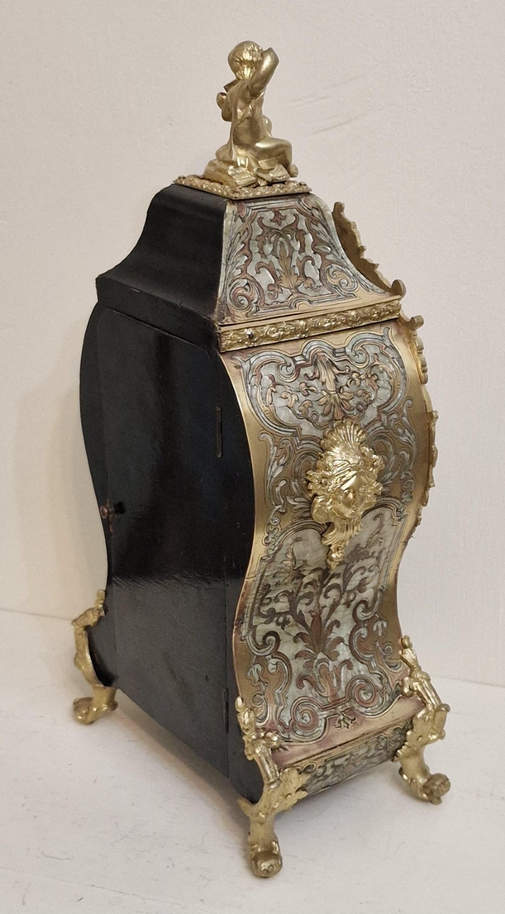 A French Rococo revival Boulle inlaid mantel clock featuring gilt brass mounts, blue Roman numerals on white enamel cartouches, and a cherub finial. View II