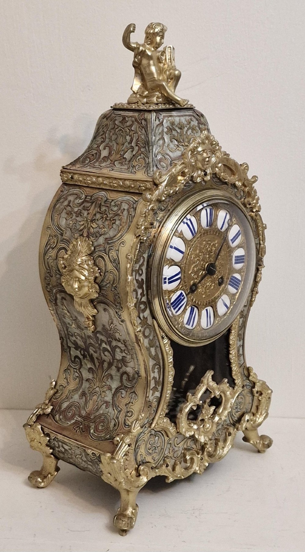 A French Rococo revival Boulle inlaid mantel clock featuring gilt brass mounts, blue Roman numerals on white enamel cartouches, and a cherub finial. View VIII