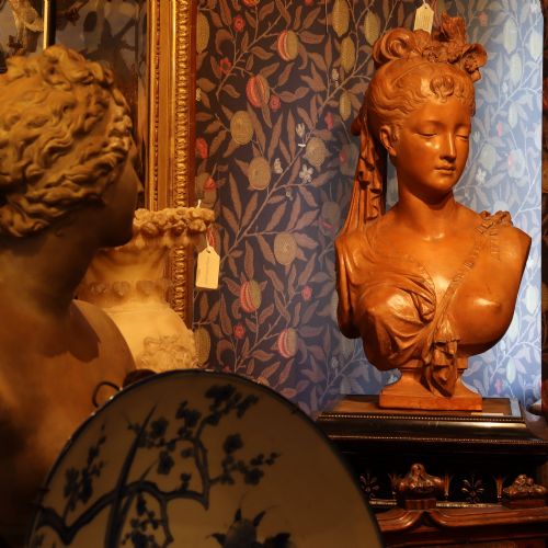 fig 2. A Neoclassical terracotta bust depicting a young woman with a floral hair arrangement and draped semi-nude torso set on an integrated base.