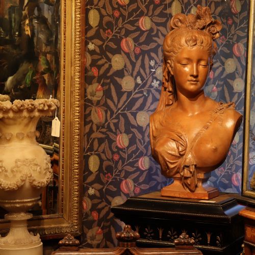 fig 1. A Neoclassical terracotta bust depicting a young woman with a floral hair arrangement and draped semi-nude torso set on an integrated base.