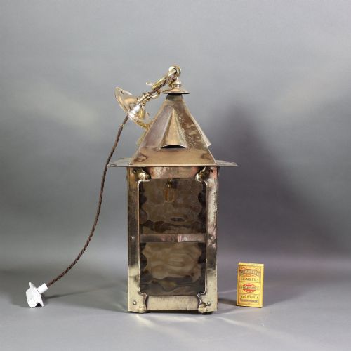 fig 2. An Arts and Crafts style brass hanging lantern featuring amber textured glass panes, a riveted square body, a pyramidal top hood, and a ceiling chain suspension.