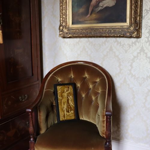 fig 1. A rectangular moulded relief ceramic tile depicting an allegorical maiden with cherubs and birds, finished in an amber translucent glaze and set in a simple dark wooden frame.