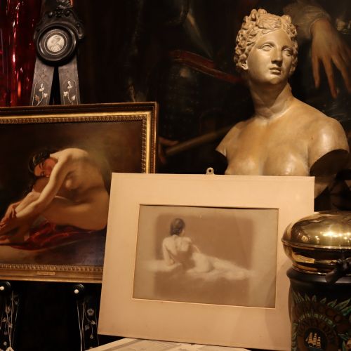 fig 1. A framed mixed media figure study on grey paper depicting the back profile of a recumbent female nude resting against a light background.