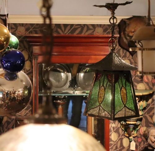 fig 1. An Arts and Crafts planished copper hanging lantern featuring leaded green, yellow, and clear glass panels suspended from a chain and floral ceiling rose.