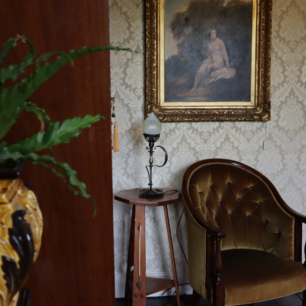 An Arts and Crafts brass table lamp featuring a hand-hammered circular base, a curved handle stem, and a flame-shaped ribbed vaseline glass shade. View II