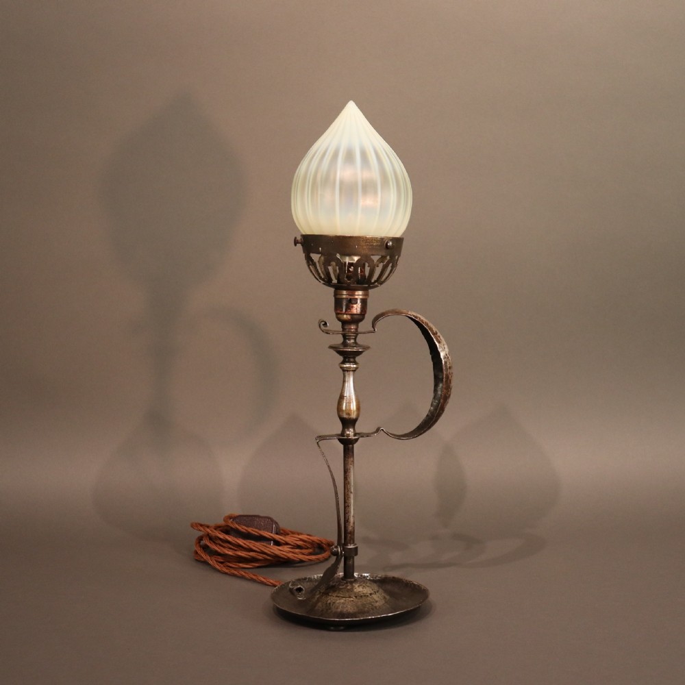 An Arts and Crafts brass table lamp featuring a hand-hammered circular base, a curved handle stem, and a flame-shaped ribbed vaseline glass shade. View IV