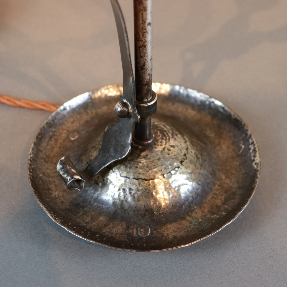 An Arts and Crafts brass table lamp featuring a hand-hammered circular base, a curved handle stem, and a flame-shaped ribbed vaseline glass shade. View VI