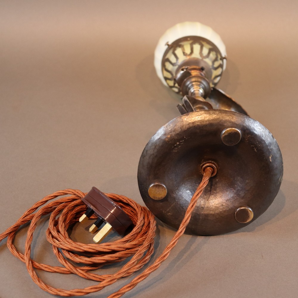 An Arts and Crafts brass table lamp featuring a hand-hammered circular base, a curved handle stem, and a flame-shaped ribbed vaseline glass shade. View VII