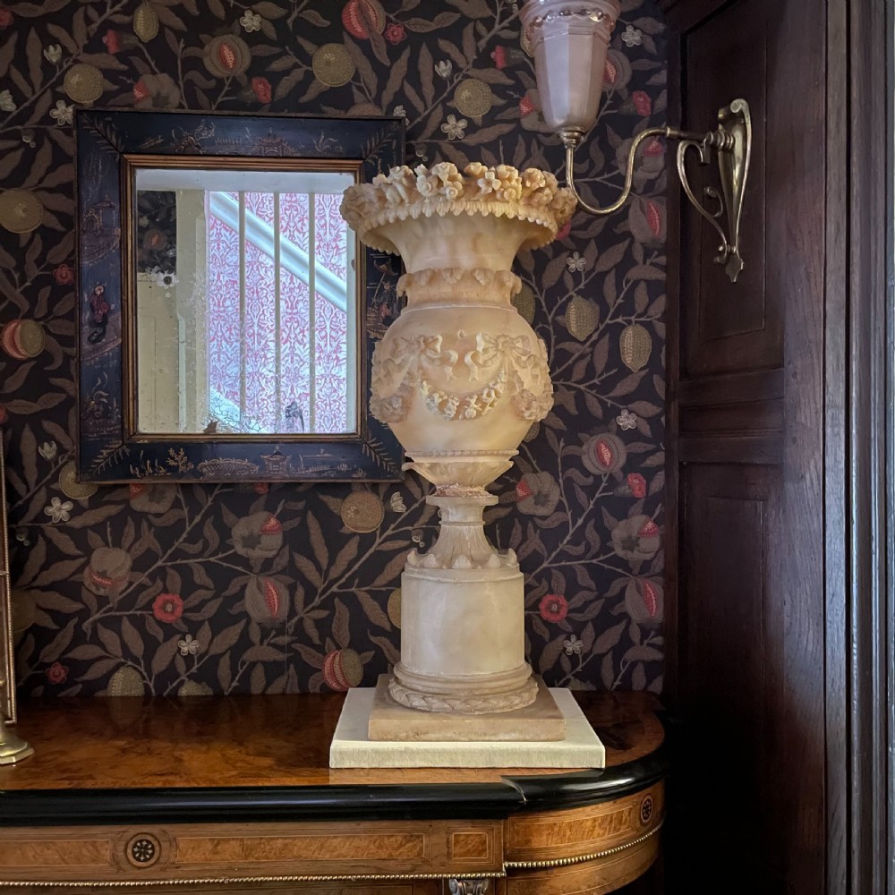A carved 19th-century cream alabaster urn featuring floral rim detailing, draped garland festoons, and a tall cylindrical pedestal base.