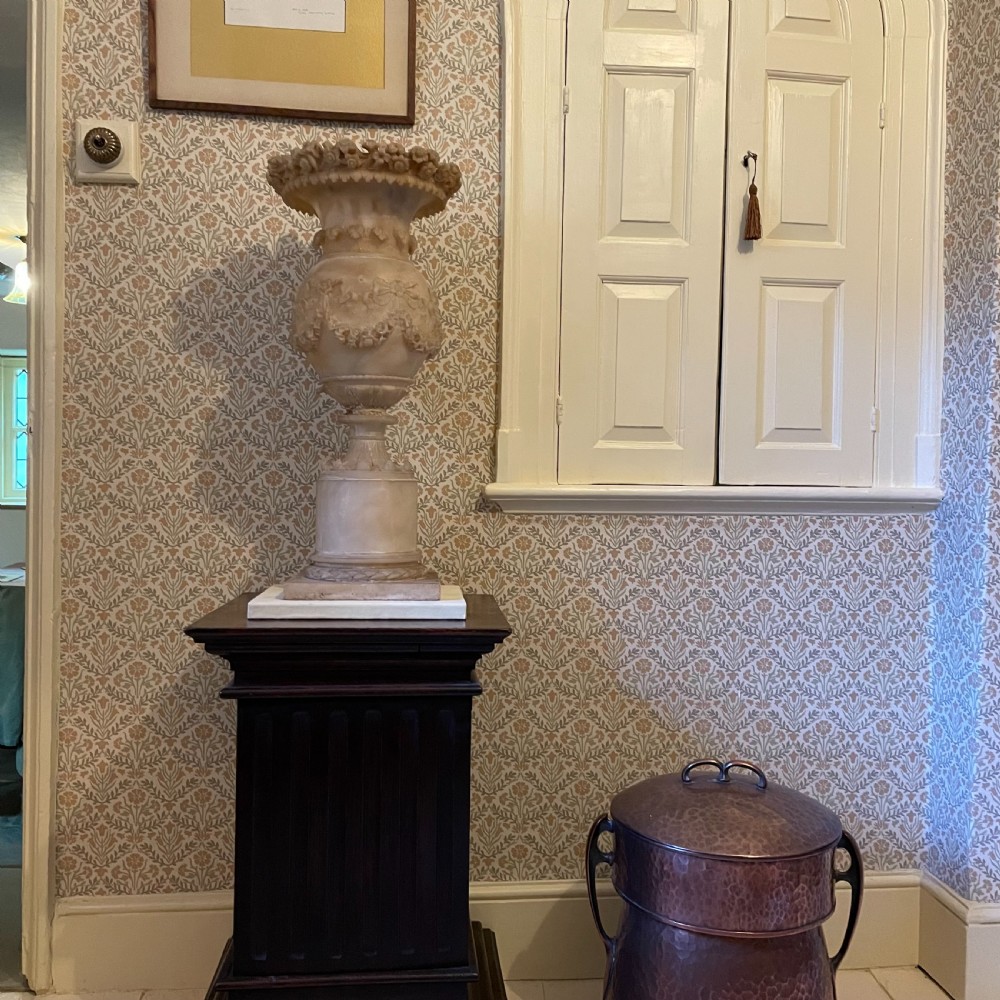 A carved 19th-century cream alabaster urn featuring floral rim detailing, draped garland festoons, and a tall cylindrical pedestal base. View III