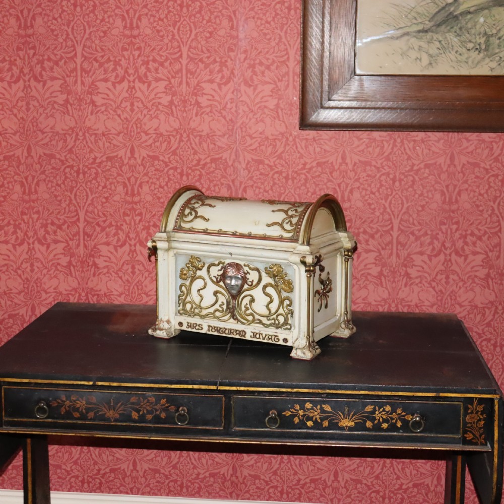 A cream-painted domed Art Nouveau casket featuring gilt metal whiplash scrollwork, a central relief mask, and a Latin inscription around the base.